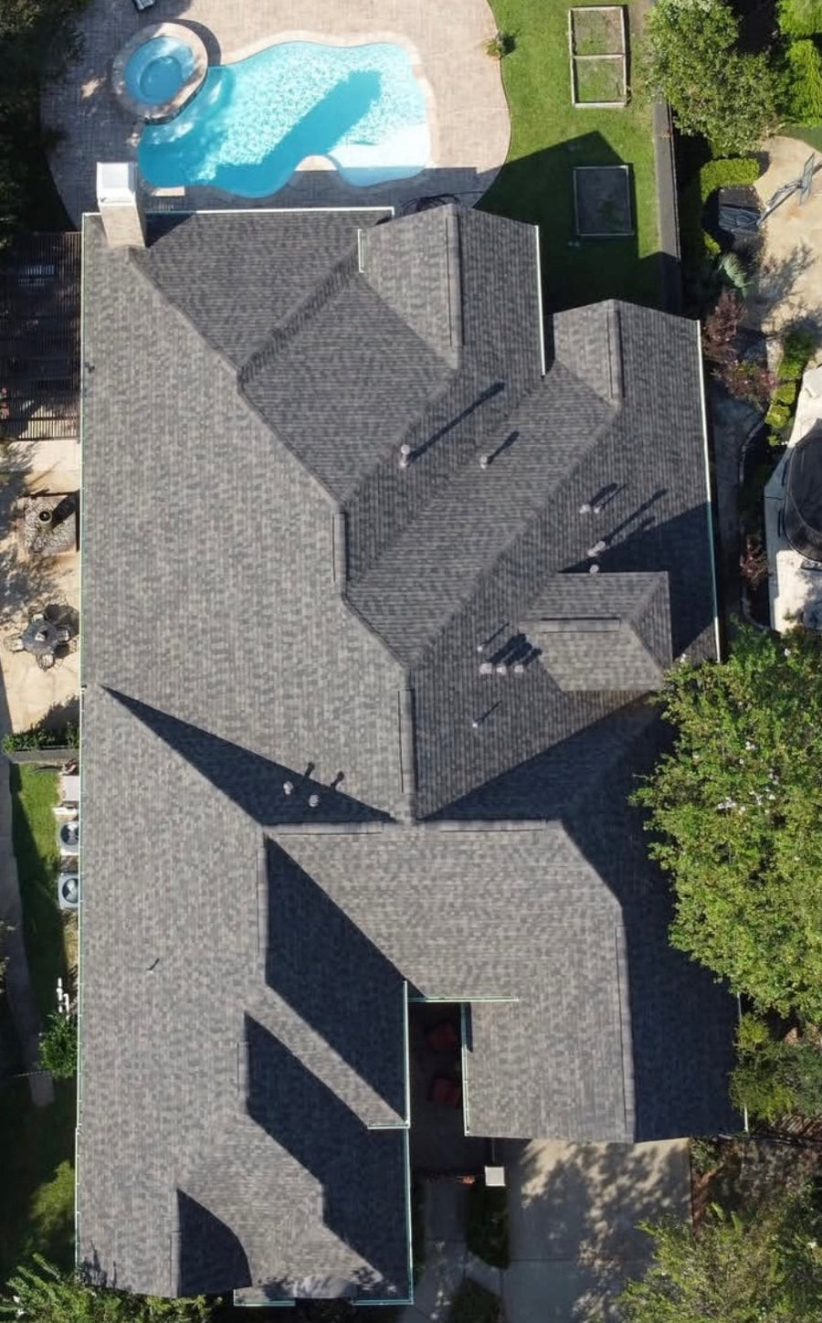 Aerial view of a residential home with a completed gray shingle roof and backyard pool area.