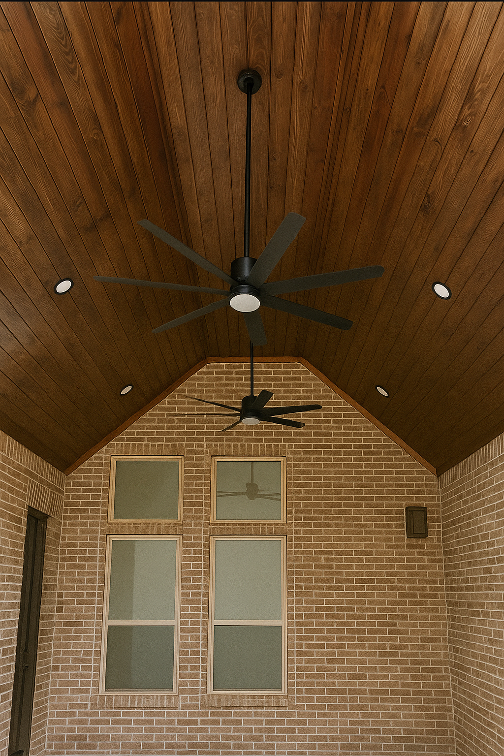 Covered backyard patio with a wood plank ceiling, recessed lights, and ceiling fans attached to a brick home.