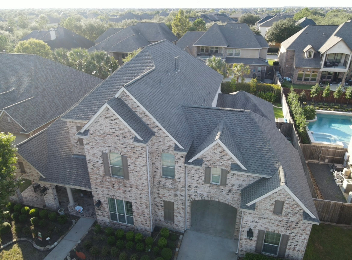 Aerial view of a two-story brick home with a gray asphalt shingle roof in a suburban neighborhood.
