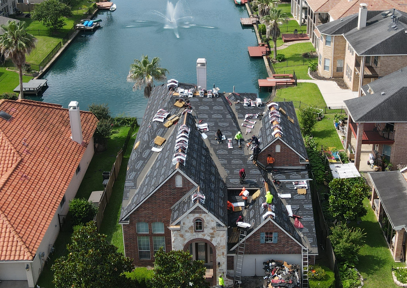 Aerial view of Prime Property Builders installing a new residential roof on a lakefront home in Sugar Land, Texas.