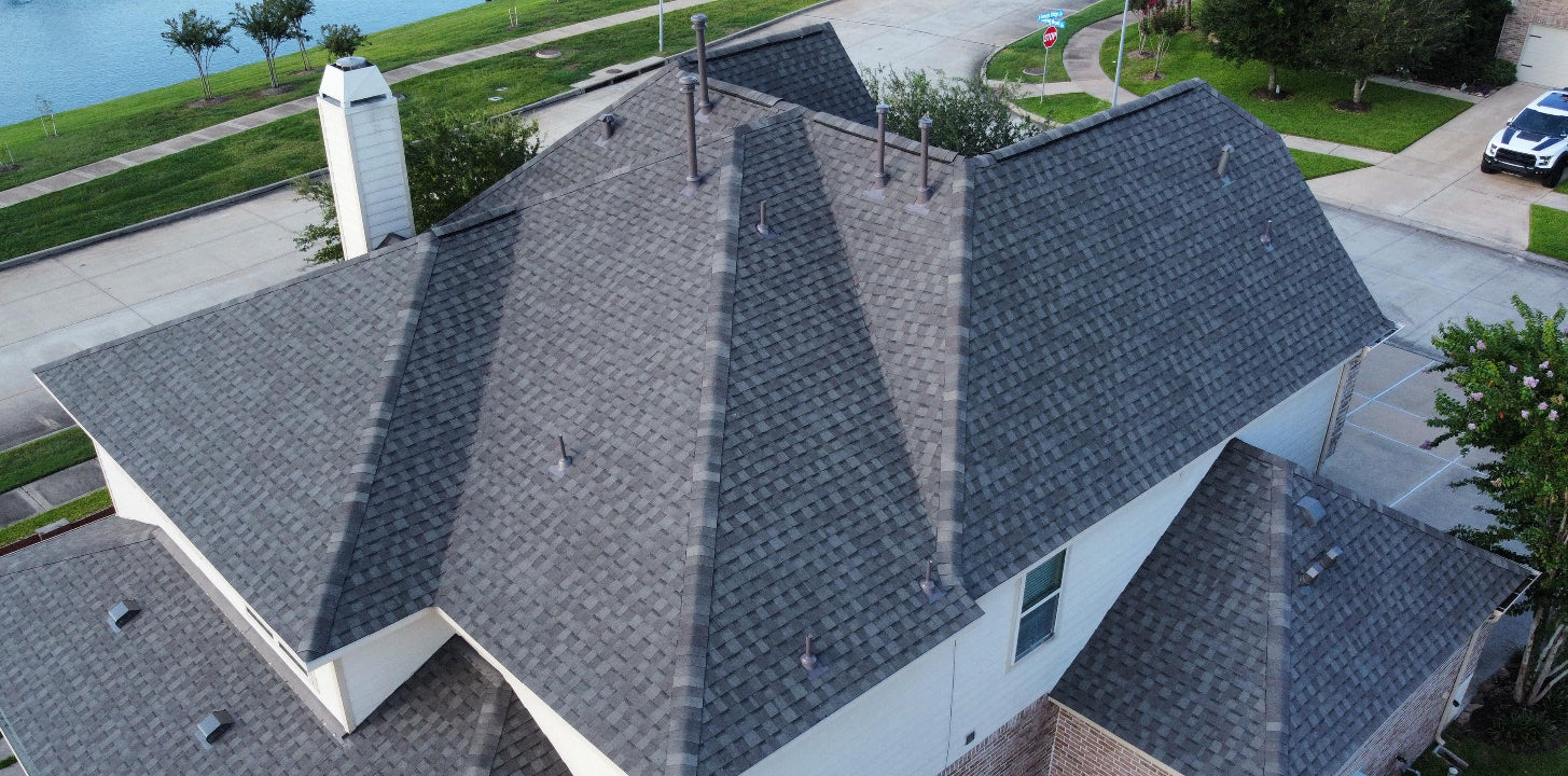 Aerial view of a residential home with an asphalt shingle roof near a street intersection in a suburban area.