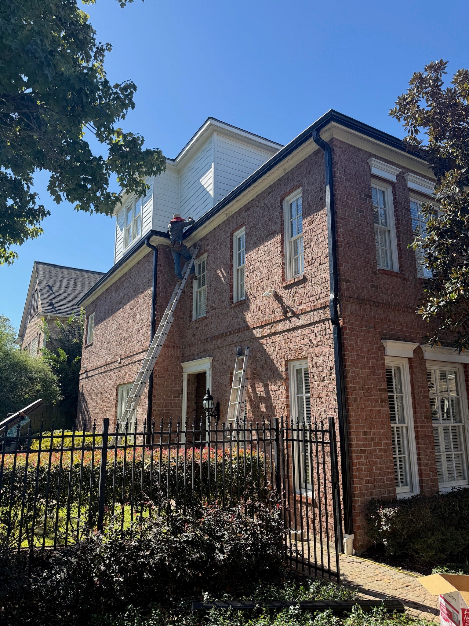 Technician installing seamless gutters on a two-story brick home in Houston as part of a residential drainage system upgrade.